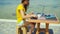 female freelancer working on laptop computer, drinking coffee from cup on beach