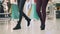 Female friends students are walking in shopping mall holding paper bags in hands enjoying season sale. Women`s legs