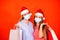 Female friends wearing surgical mask and Christmas hat holding shopping bags on a vivid red orange background