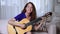 Female guitar teacher playing and singing with acoustic guitar at home.