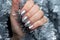 Female hand with beautiful holiday manicure - silver glittered nails on Christmas tinsel background. Selective focus