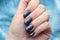 Female hand with beautiful manicure - dark gray blue glittered nails on blue knitted sweater fabric background