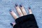 Female hand in black knitted gloves mitts with beautiful manicure - dark blue glittered nails on knitted background