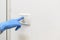 A female hand in a blue latex glove turns on or off the light in an apartment or in a house. Antibacterial protection. Quarantine