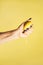 Female hand with blue nails hold fresh lemon isolated on yellow. Squeeze out juice. Finger crush. Vertical, copy space