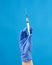 Female hand in a blue sterile rubber glove holds a white syringe