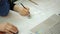 Female hand of a cartographer draws on urban plan of building with a pencil, near eraser and a laptop on table.