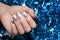 Female hand with Christmas nail design. Silver nail polish manicure. Female hand on blue New Year tinsel background