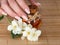 Female hand with classic manicure, jasmine flowers and essential oil on reed mat. Woman touches a bottle by with her