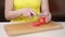 Female hand of a cook cuts a red tomato close up on a wooden board.