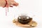 Female hand covers a glass teapot standing on a wooden stand on a white table