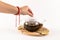 Female hand covers a glass teapot standing on a wooden stand on a white table