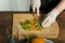 A female hand cuts a knife on a wooden kiwi plate into pieces.