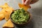 Female hand dips chips slice in guacamole, close up