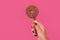 Female hand with doughnut ice cream on a stick on pink background in studio