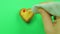 Female hand draws a heart-shaped cookie on a green background with a red tube frosting funny emoticons.