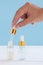 Female hand with Dropper of essential oil, aromatherapy essence, beuty serum or medicinal liquid on beige background. Unbranded