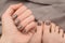 Female hand and feet with brown nail design. Beige nail polish manicure and pedicure on brown fabric