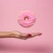 Female hand with flying delicious donut on pink background.