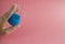 Female hand with French manicure in medicine glove holds blue cosmetic medical jar for vacuum facial massage on pink background.