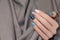 Female hand with glitter nail design. Blue nail polish manicure. Woman hand on grey fabric