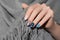 Female hand with glitter nail design. Blue nail polish manicure. Woman hand hold grey wool shawl