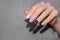 Female hand with glitter purple nail design. Pink nail polish manicure. Rose manicure on gray background