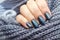 Female hand with gray knitted scarf with beautiful manicure - blue glittered nails