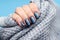 Female hand in a gray knitted sweater fabric with beautiful manicure - dark gray blue glittered nails