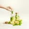 Female hand with green manicure making healthy drink lemonade in bottles with lemon, ginger and mint leaves at light background.