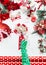 Female hand in green polka dot blouse making festive Christmas funky bow on white desktop with various red holiday decoration,