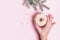 Female hand hangs Christmas bauble decoration made of donut on pink background. Christmas creative concept