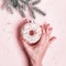 Female hand hangs Christmas bauble made of glazed donut on pink background. Christmas creative concept