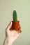 Female hand hold small cactus in orange pot at beige background. Urban jungle. Minimal and simple modern lifestyle