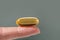 Female hand holding a big yellow capsule of nutritional supplement. Food supplement, vitamin D, omega, vitamin C.