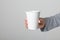 Female hand holding blank empty take away paper cup on neutral grey wall background