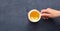 Female hand holding a cup of tea with lemon top view on a dark stone background