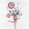 Female hand holding flowers bunch with ribbon on white desktop with cup of tea and women`s things. Top view. Flat lay