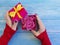 Female hand holding gift box with bow romantic birthday congratulation , rose flower on blue wooden background