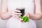 Female hand holding glass of green chlorophyll drink with mint leaves on a light pink background