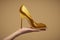 Female hand holding gold-colored high-heeled shoe