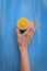 Female hand holding half a lemon on a background of a wooden table painted in blue color