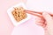 Female hand holding japanese natto beans with wooden chopsticks on pink background, top view.