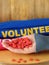 Female hand is holding many little hearts on a wooden background. Volunteer uniform in the background