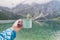 Female hand holding mint color enamel cup. Crystal clear lake and mountains. Tatra National park, Poland. Famous lake