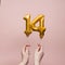 Female hand holding a number 14 birthday anniversary celebration gold balloon