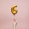 Female hand holding a number 6 birthday anniversary celebration gold balloon