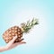 Female hand holding pineapple at light blue background. Summer tropical fruits concept. Copy space for your design