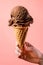 Female hand holding scoop of crave-worthy dark rich chocolate ice cream with velvety texture in waffle cone with melting dripping