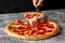 Female hand holding serving paddle with slice of pepperoni pizza with melted cheese and jalapeno